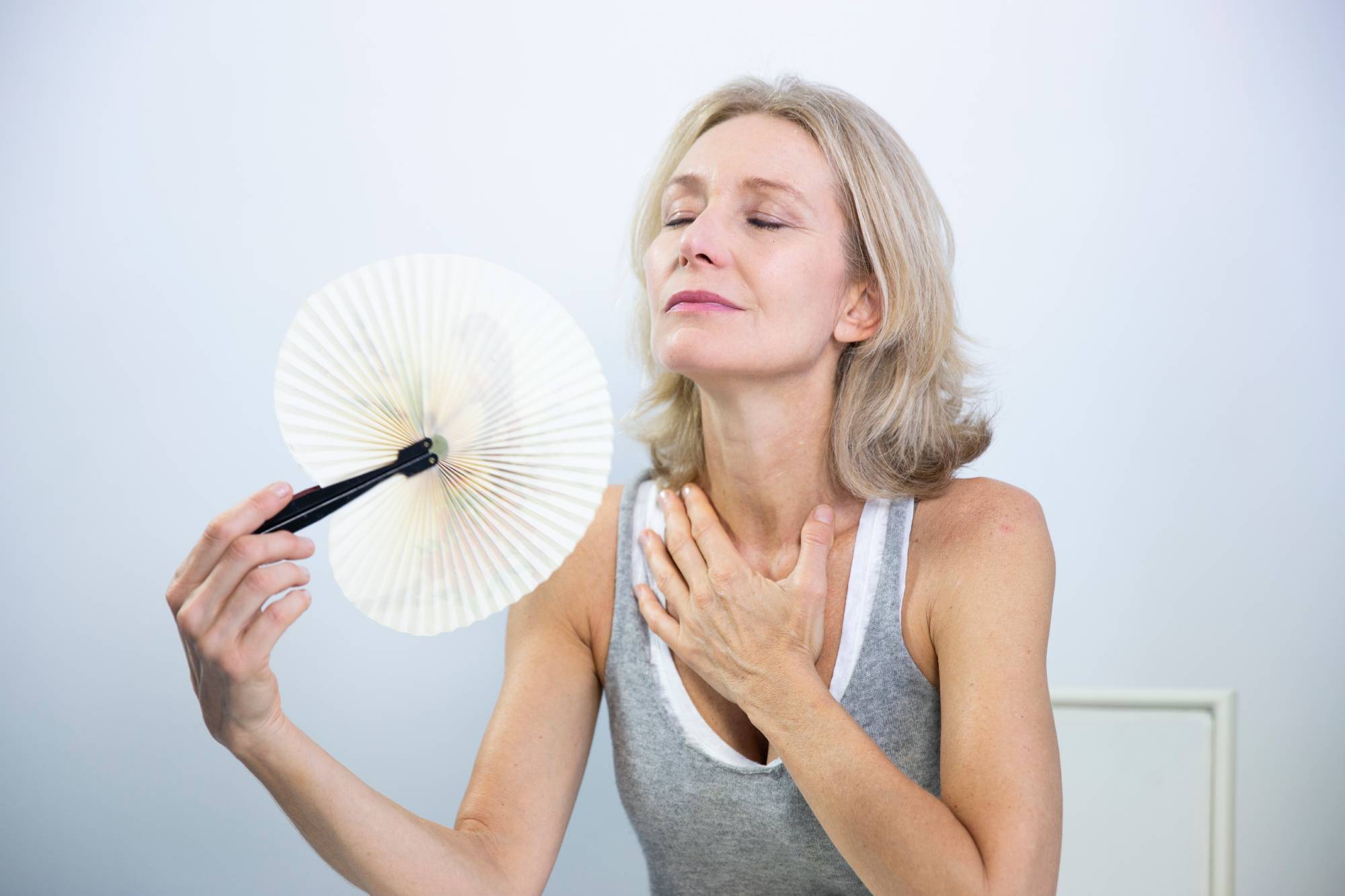 middle-aged woman with fan cooling herself down during hot flushes