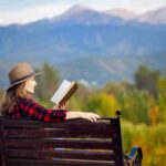 woman reading a book on a bench in Canada with the mountains in the background