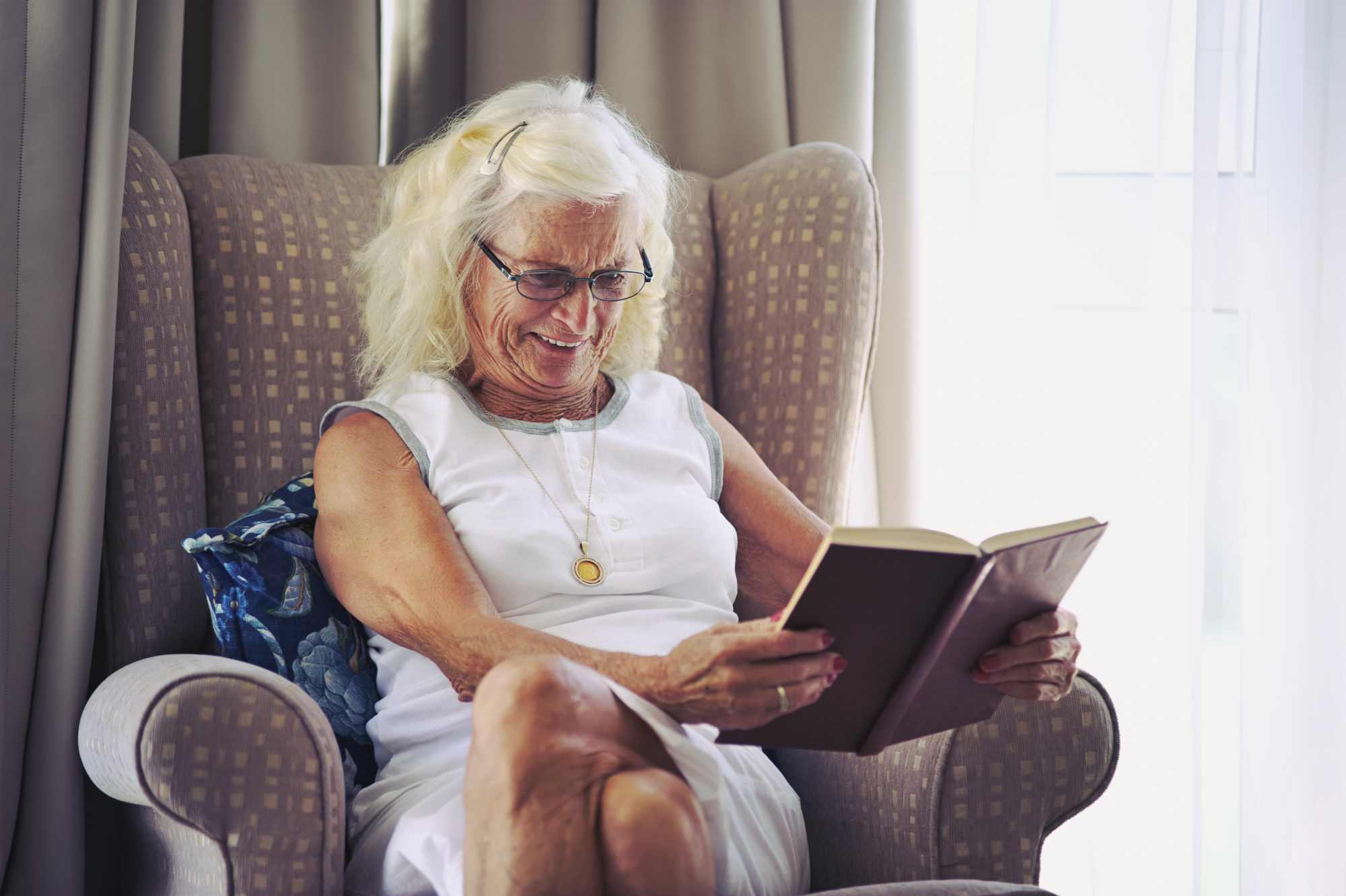 An old lady sitting on her couch and enjoying her book