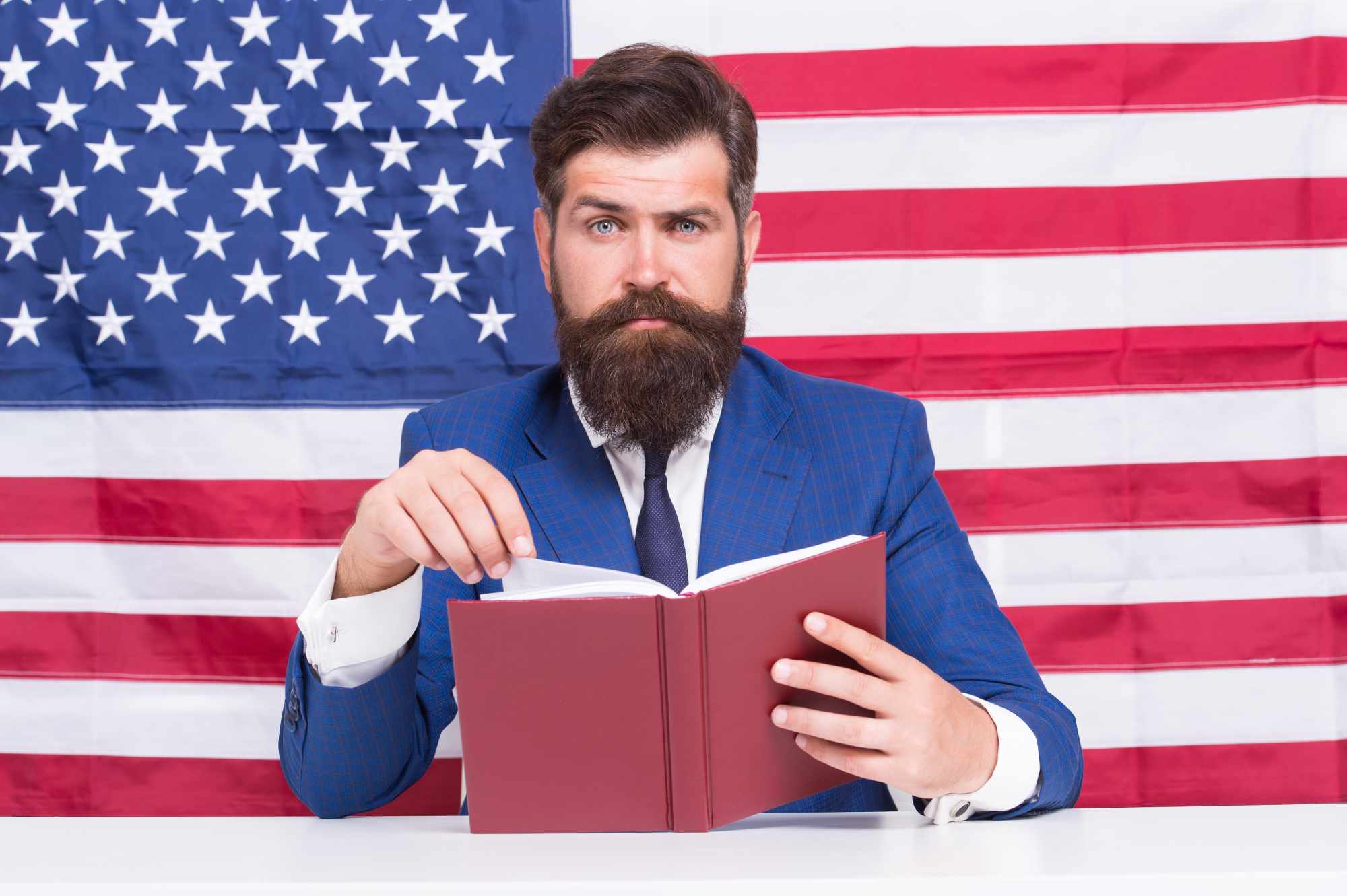 Man reading book with American flag behind him