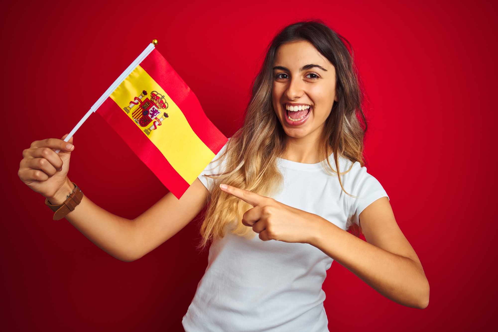Young beautiful woman holding spanish flag over red isolated background very happy pointing with hand and finger